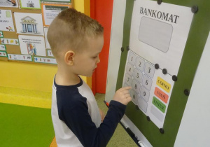 Chłopiec wypłaca pieniądze z bankomatu.